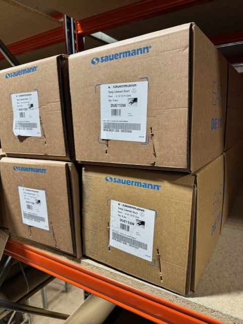 Stack of cardboard boxes with 'sauermann' branding on a metal shelf.